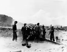 A large artillery piece fires as several soldiers look on