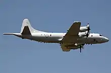 A grey, four engined aircraft viewed from below while it is in flight