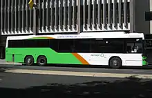 Light green, orange, and white bus stopping in front of multi-story building. (from Transport)