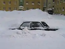 A car buried in a snowdrift with only the left side, from just below the windows, visible