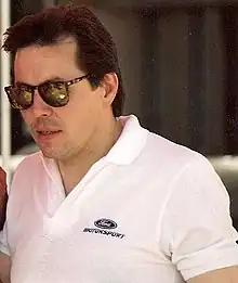 Alan Kulwick wearing black sunglasses over his eyes and a white T-shirt with a car company's logo on its left