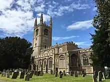 A stone church seen from the southeast with Perpendicular windows, embattled parapets, and a west tower with tall pinnacles