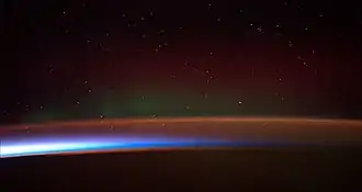 Image 25Earth's atmosphere as it appears from space, as bands of different colours at the horizon. From the bottom, afterglow illuminates the troposphere in orange with silhouettes of clouds, and the stratosphere in white and blue. Next the mesosphere (pink area) extends to just below the edge of space at one hundred kilometers and the pink line of airglow of the lower thermosphere (invisible), which hosts green and red aurorae over several hundred kilometers. (from Earth)