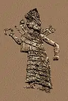 Goddess Ishtar/Inanna. She wears a long, flounced dress, a hat decorated with horns and a headed collar. She is extending a ring in her right hand and has club-like weapons in her back.