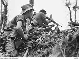 Black and white photograph of two Australian soldiers taking cover behind an embankment. One is aiming his rifle over the top.