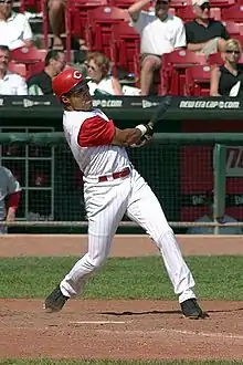 A man in a white baseball uniform with red undersleeves and cap