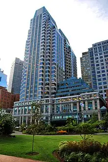 Ground-level view of a complex of skyscrapers; the tallest building is on the left, with a light tan facade and a green-gray trapezoidal cap.