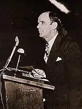 A man stands at a podium with a light colored object above his head