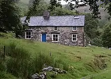 A colour photograph of a stone cottage on a hill