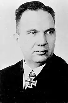 A man wearing a black military uniform with an Iron Cross displayed at the front of his uniform collar.