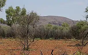 A dark-red sandstone hill emerging from bushes