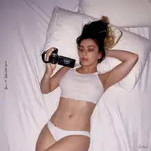 Charli XCX lying in bed and holding a camera