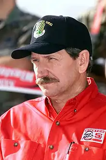 Dale Earnhardt wearing a black baseball cap with a military logo and a red shirt with the top button undone