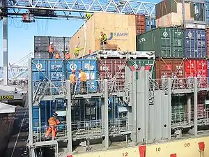 Dockworkers securing containers on a ship with steel lashing bars and turnbuckles