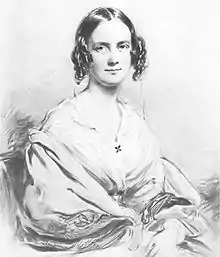 Three-quarter length portrait of woman aged about 30, with dark hair in centre parting straight on top, then falling in curls on each side;  she smiles pleasantly and is wearing an open-necked blouse with a large shawl pulled over her arms