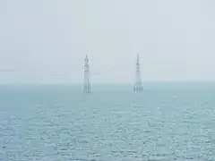 Two electrical transmission towers standing in a featureless expanse of water under a hazy sky