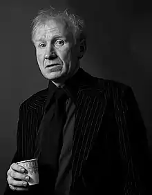 Linden wearing a suit and holding a cup