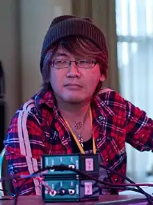 A bespectacled Hiroki Kikuta, in a plaid shirt and a stocking cap