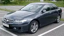 A blue saloon car parked in a bay in an empty car park. The licence plate is blank.