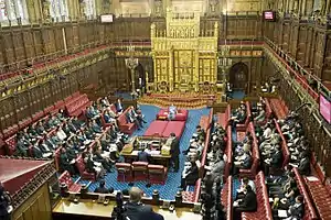 Wood-panelled room with high ceiling containing comfortable red padded benches and large gold throne