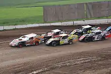 a single car leads a group of other cars which are being driven in double-file