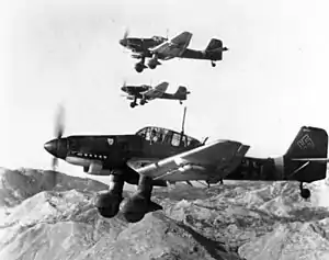 a black and white photograph of seven aircraft in flight over a smoky battleground