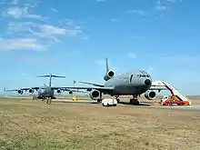 Two large gray jet aircraft on roomy ramp surrounded by grass, both angled away from the runway. The one closer to camera is three-engined, while the one further in the background is four-engined.