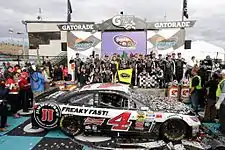 a parked race car covered with confetti and surrounded by celebrating team members