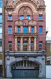 Narrow four storey red building above a wide archway