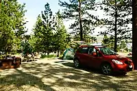 Campsite with a red car next to a tent in a small clearing surrounded by trees