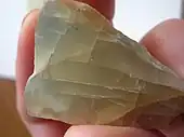 A chunk of grayish yellow moonstone which shows fracture lines and a blue glow in some portions.