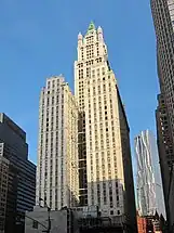 Very tall skyscraper with trees in the foreground and a tall but significantly shorter building to the left