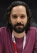 A 36-year-old man with curly black hair smirking at the camera.