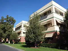 Three story building with green stripes surrounded by some trees