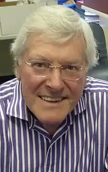 A 71-year-old man with white hair and glasses smiling at the camera.