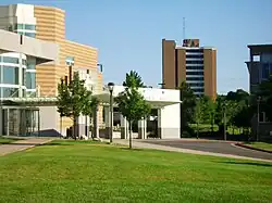 Buildings on a college campus. In the rear is a high-rise brick dormitory building. Mounted on it is a guyed steel mast with FM antennas.