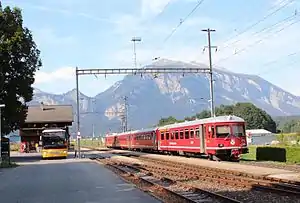 Two-story building with gabled roof next to multiple tracks and platforms and a red train