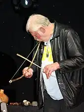 Man playing a heterochord musical bow, using his mouth for a resonator. Heterochords have strings made of a different material than the rigid part of the bow.