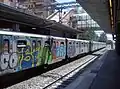 A side view of the 1990 built MB100 cars on a Laurentina bound train stopping at EUR Magliana covered with graffiti.