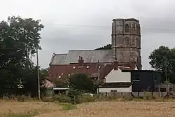 Stone building with square tower above smaller buildings.