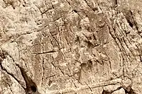 Sarpol-e Zahab, relief I. Beardless warrior with axe, trampling a foe. Sundisk above. A name "Zaba(zuna), son of ..." can be read. He is usually considered as a ruler of the Lullubi, but he could be a ruler of the Kingdom of Simurrum, son of Iddin-Sin.