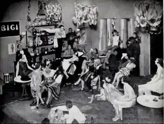 scene in an Italian club with young man standing on the bar, watched by a seated young woman, both surrounded by other people