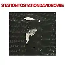 A black-and-white photo of a man stepping into a room filled with cylindrical bars, imposed onto a thick white border with "STATIONTOSTATIONDAVIDBOWIE" in red text at the top