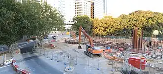 Construction site with an excavator sitting there. The station box has begun to be excavated.