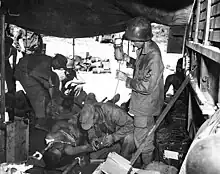 Medics treat a pair of injured men in a tent in the middle of a jungle