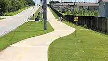 Photograph of a concrete urban trail running alongside a road