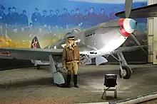 A restored grey fighter plane in a museum. Its nose is painted in the French tricoleur.