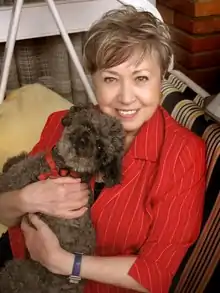 photo of a middle-aged woman with short hair, wearing a red blouse, and holding a dog